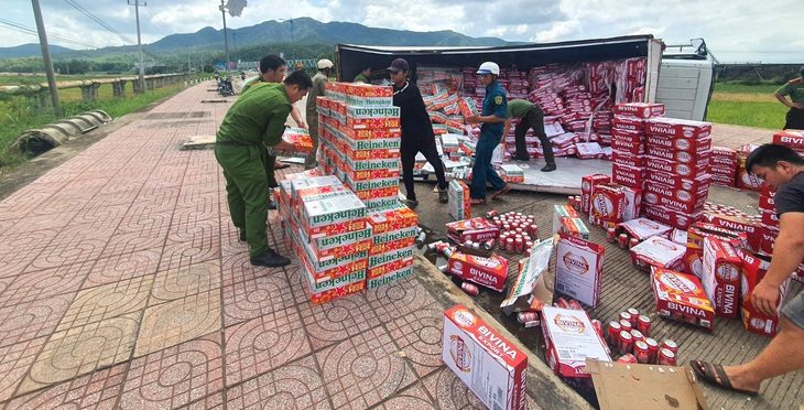 Hàng trăm thùng bia trên xe tải bị đổ xuống đường, công an hỗ trợ tài xế gom bia - Ảnh: Công an cung cấp